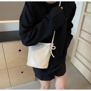 Detail einer cremebeigen Beuteltasche mit großem Perlen-Schleifen-Anhänger am Riemen