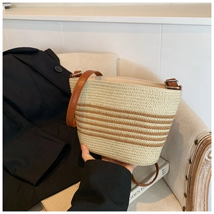Close-up of striped straw bucket bag with brown leather strap on soft fabric