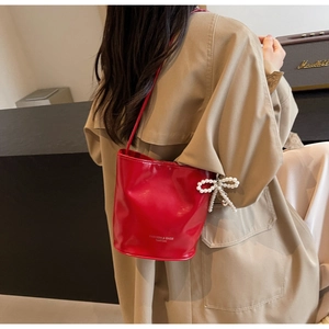Detail der roten Beuteltasche mit weißem Perlen-Schleifen-Anhänger und glatter PU-Oberfläche