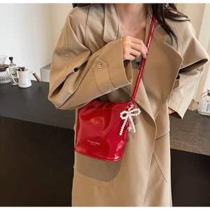 Detail der roten Lackleder-Eimertasche mit Perlenbogen-Anhänger am Trenchcoat