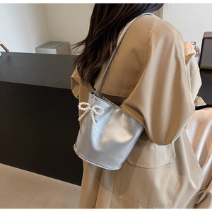 Detail der silbernen Eimertasche mit weißer Perlen-Schleife auf Metallic-Finish