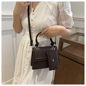 Detail of dark chocolate crossbody bag with knotted handle and mini coin pouch on a white dress