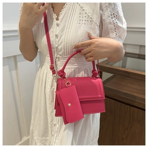 Detail of rose red crossbody bag with knot handle and mini purse on white lace dress
