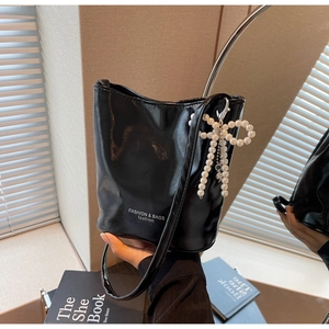 Detailed view of black glossy bucket bag featuring white pearl bow charm and shoulder strap