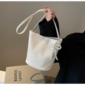 Detail der cremeweißen Beuteltasche mit Perlen-Schleifen-Anhänger und Herz-Akzent