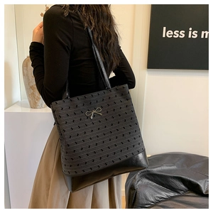 Detail view of a black polka dot tote bag with a gold bow accent on a minimalist setup
