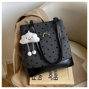 Detail of grey polka dot tote bag with metal bow and plush cloud charm on a book