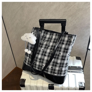 Detailed view of checkered tote bag with plush charm on a white suitcase for travel