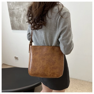 Detail view of large brown vintage leather bucket bag worn by model in minimalist setting