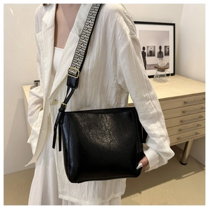 Detail of black faux leather bucket bag with retro texture and patterned wide strap