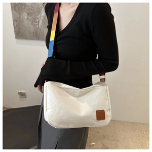 Détail du sac bandoulière en toile avec sangle colorée et écusson logo en cuir sur modèle