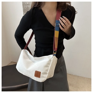 Detail of white canvas crossbody bag with multi-color rainbow wide shoulder strap and leather patch