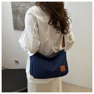 Modèle portant un sac bandoulière en toile bleu foncé avec logo en cuir et sangle stylée