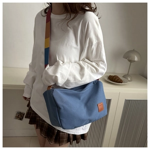 Détail du sac bandoulière en toile bleue doté d'une sangle arc-en-ciel rayée dynamique