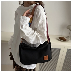 Detail of black canvas messenger bag featuring a colorful striped wide shoulder strap