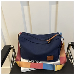 Detail of navy canvas messenger bag with colorful striped strap and leather logo patch
