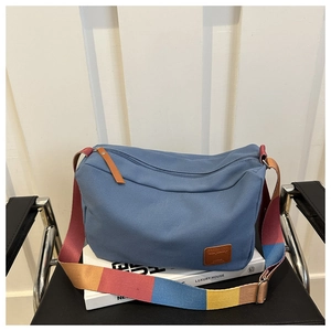 Detail of blue canvas tote featuring adjustable colorful striped strap and leather logo
