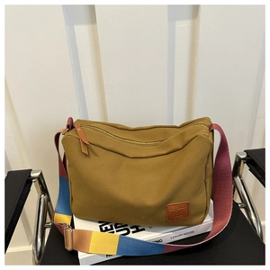 Detail of mustard yellow canvas bag featuring multi-color striped strap and brown leather logo