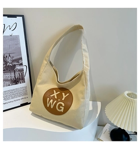 Detail view of beige canvas tote bag with a circular leather patch on a modern display stand