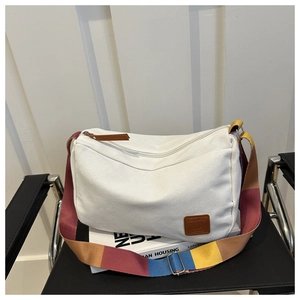 Detail of white canvas tote featuring a vibrant multi-color striped wide shoulder strap