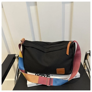 Detail of black canvas pillow bag with a colorful rainbow strap and leather logo patch