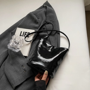 Detail of glossy black bucket bag with pearl bow and white fashion text branding