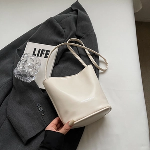 Detail view of cream leather bucket bag with fashion text on a gray blazer backdrop