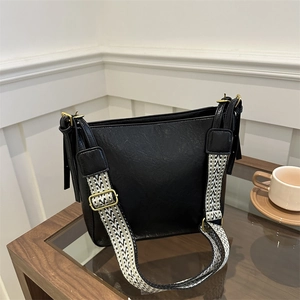 Large black bucket bag with textured leather and geometric wide strap on a table