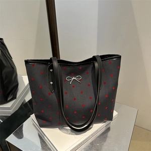 Sac cabas gris en toile à pois rouges avec boucle nœud argentée posé sur livres