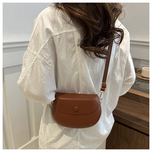 Brown matte leather saddle bag with round buckle shown worn as a crossbody by a model