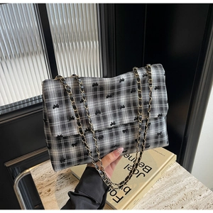 Détail d'un sac à carreaux noir et blanc avec broderie nœud et chaîne en métal doré