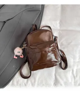 Close-up of brown glossy patent leather mini backpack with cute pink plush keychain charm