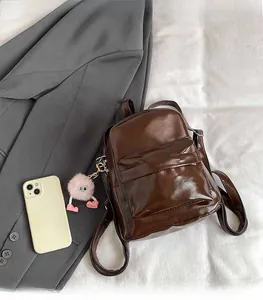 Deep brown faux leather mini backpack with plush charm and smartphone for scale