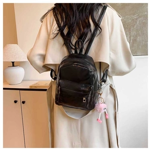Mini sac à dos en cuir noir avec pompon rose porté par un mannequin dans un intérieur