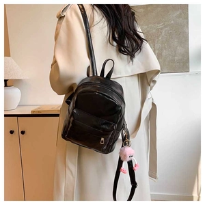 Vue arrière d'un mini sac à dos noir compact avec un charm pompon rose sur un mannequin