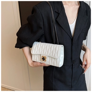 Detail of white quilted crossbody bag with a gold clover clasp on a black blazer