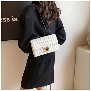 Close-up of a white quilted shoulder bag featuring a gold floral lock and chain strap