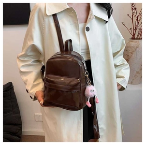 Détail d'un mini sac à dos marron foncé brillant avec un charme en peluche rose