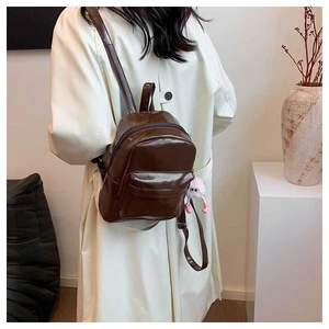 Detail of brown PU leather mini backpack with plush pendant worn with white trench coat