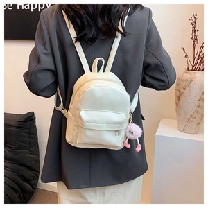 Mini sac à dos en cuir blanc porté avec un charmant pompon en peluche rose