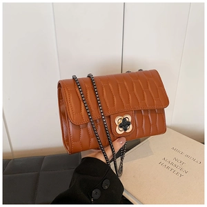 Close-up of caramel quilted leather bag with chain strap and gold clover buckle lock