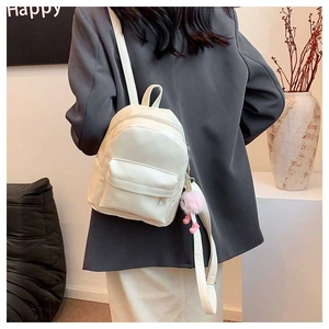 Back view of a mini white backpack with a pink plush charm on a model in a modern room