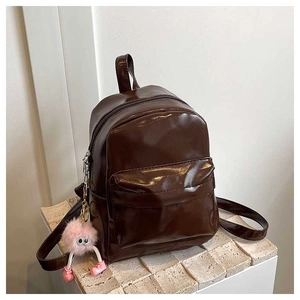 Détail d'un mini sac à dos marron foncé brillant avec un charme pompon rose