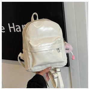 Détail d'un mini sac à dos crème en similicuir brillant avec pompon rose