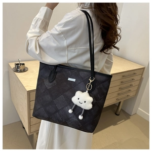Detail of black quilted tote bag with a white cloud charm worn on a model's shoulder