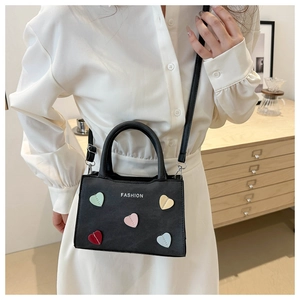 Detail of a black mini crossbody bag with colorful heart patches and fashion text