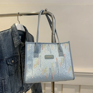 Light blue quilted tote bag with colorful wave embroidery and fashion label on a hanger