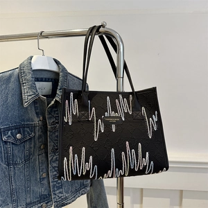Black tote bag with colorful wave embroidery and embossed texture on a metal hanger