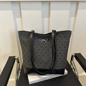 Gray canvas tote bag with black heart prints and silver bow pendant on a minimalist chair
