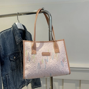 Pink tote bag with textured colorful embroidery and leather straps hanging on hanger